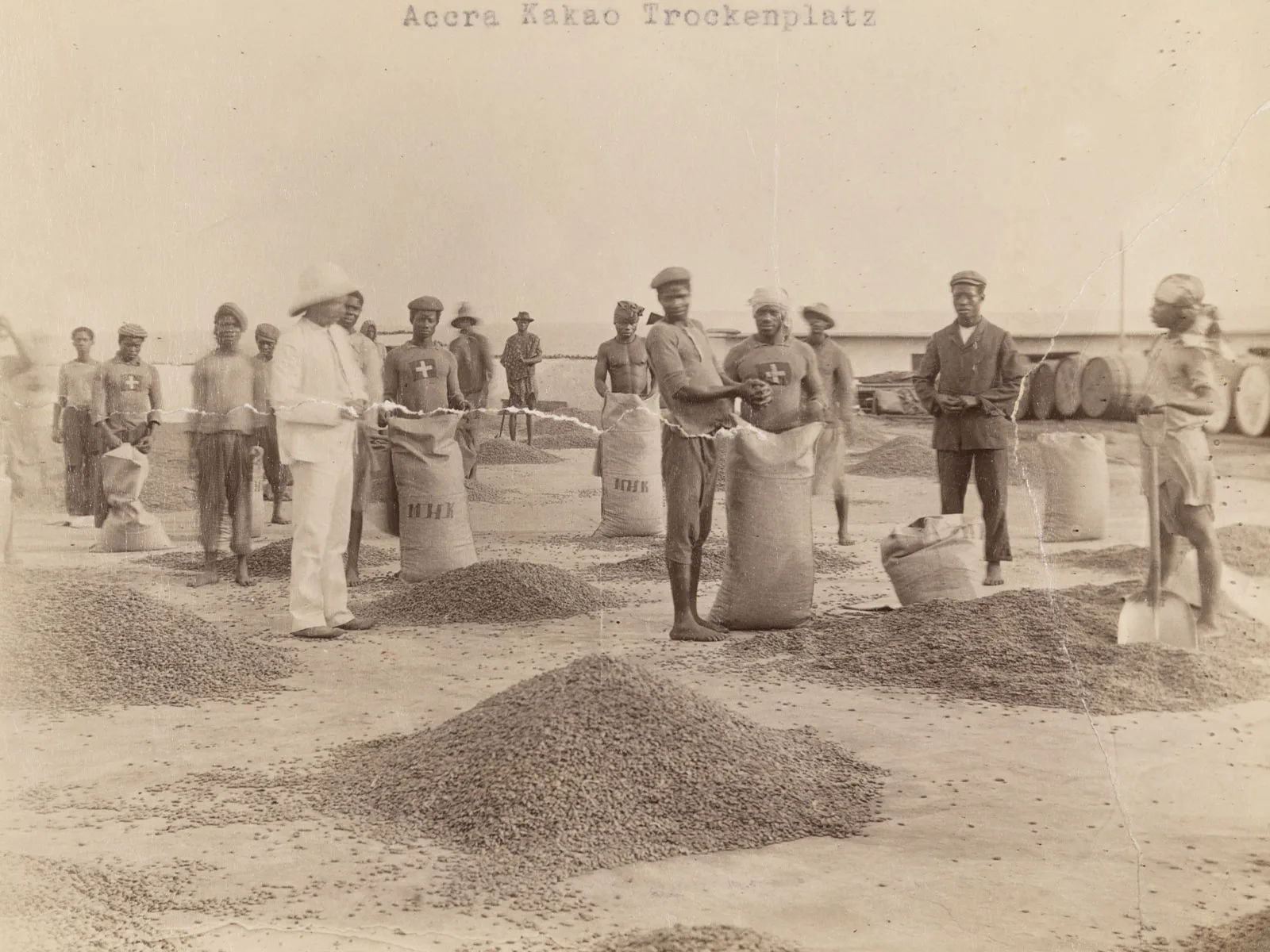 Local workers and a supervisor dressed in ‘colonial whites’ at a cocoa drying area run by the Basel Mission Trading Company in Accra in what is now Ghana (1904/1905).